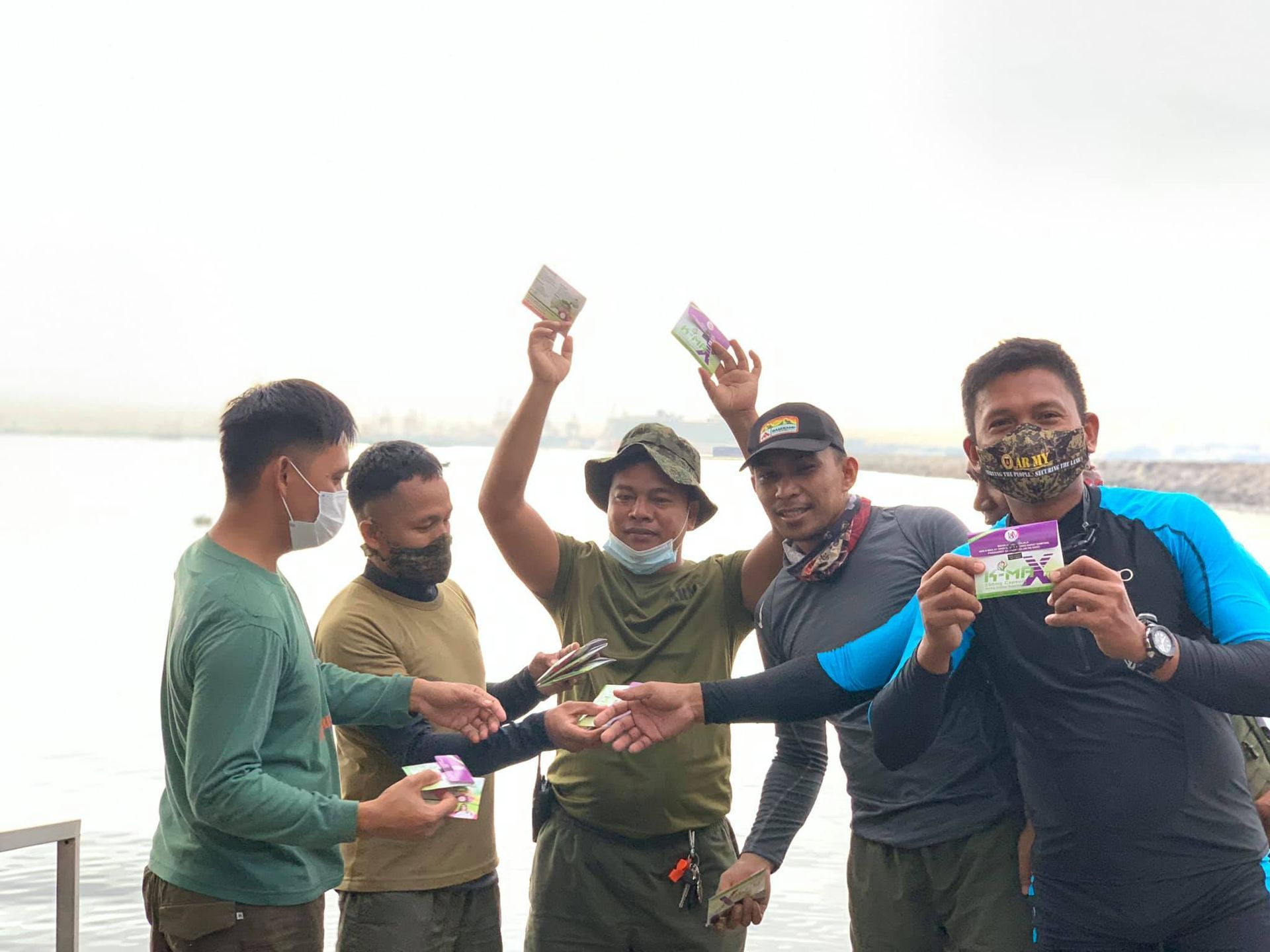 A group of men wearing face masks are standing next to each other in front of a body of water.