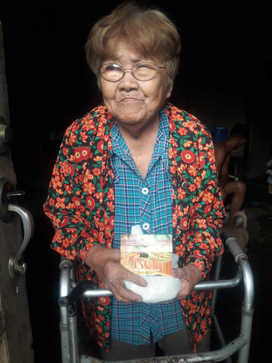 An elderly woman is using a walker and holding a bowl of food.