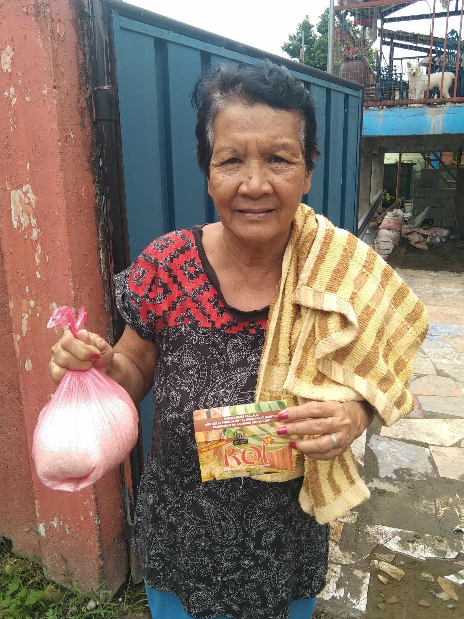 An elderly woman is holding a bag of food and a towel.