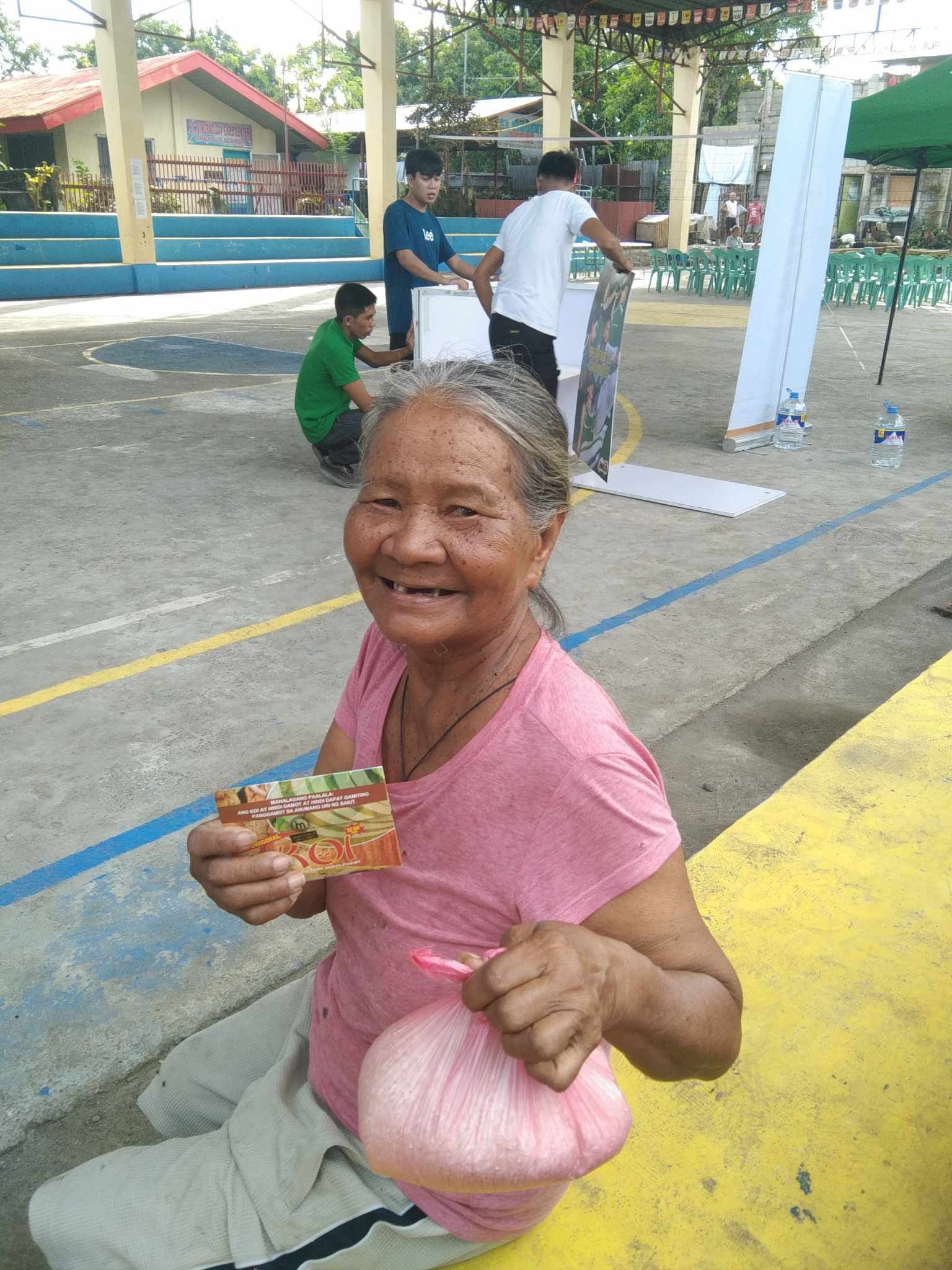 An elderly woman is sitting on a bench eating a slice of pizza.