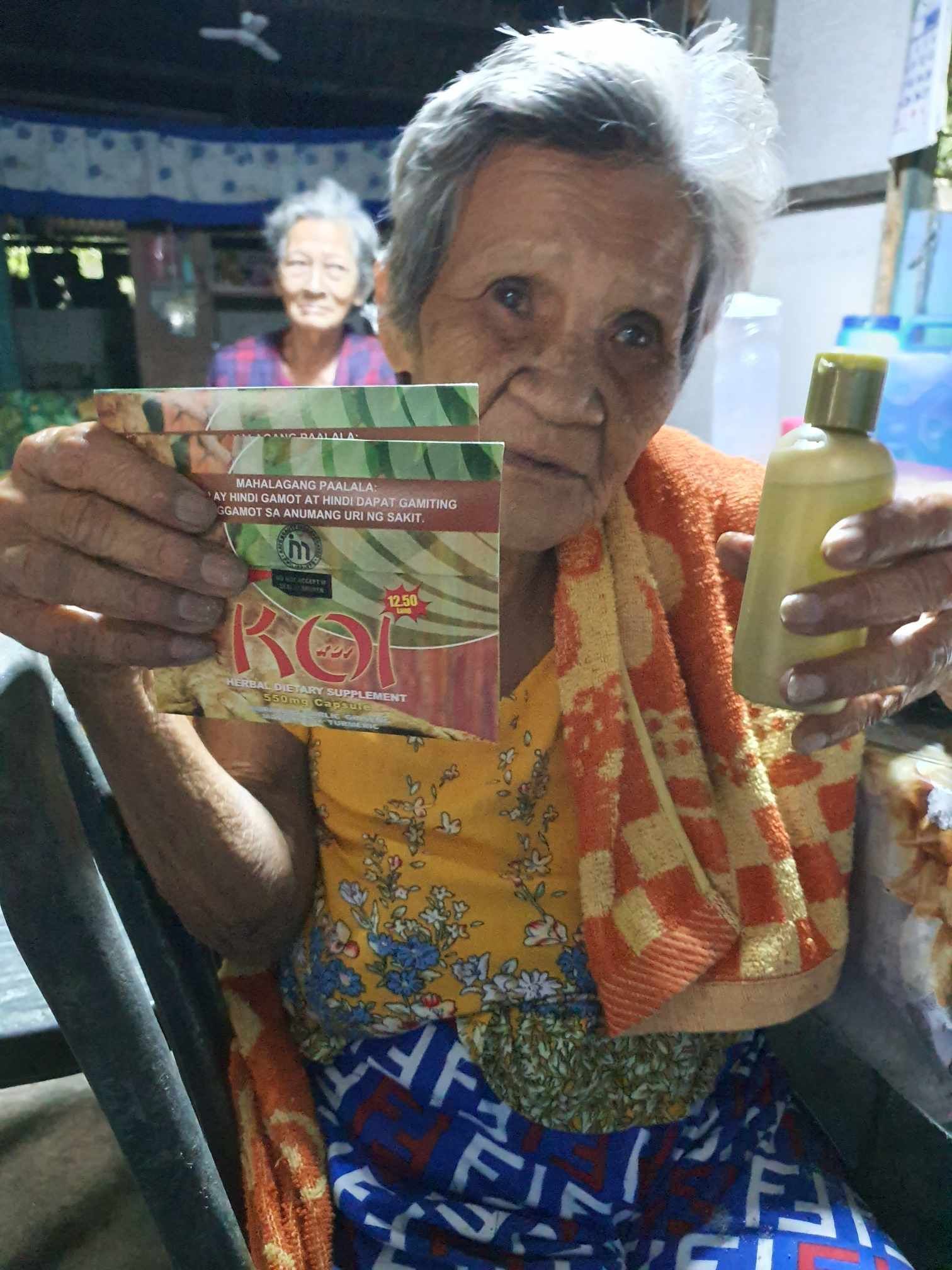 An elderly woman in a wheelchair is holding a bottle and a card.