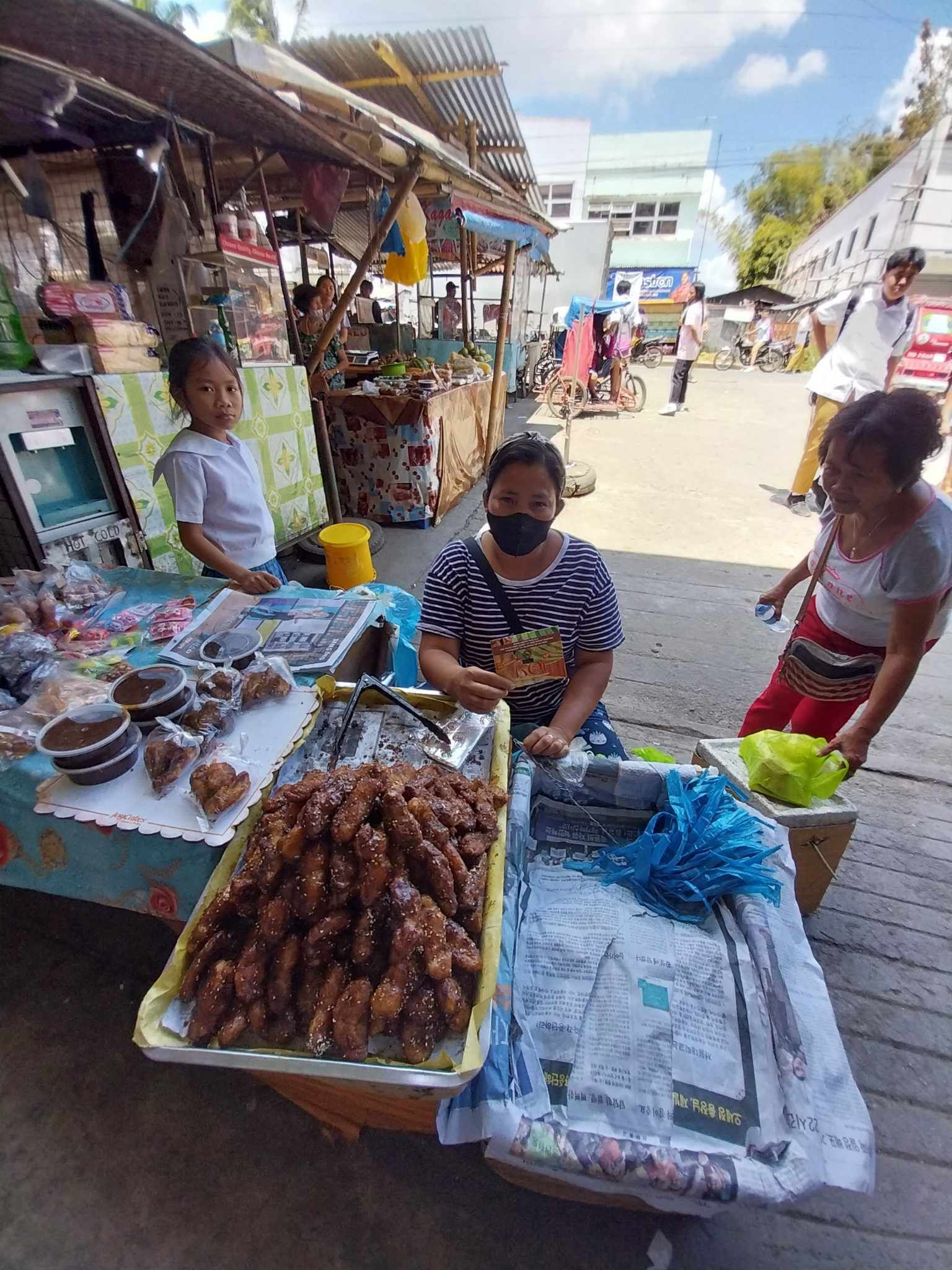 A woman wearing a mask is selling food at a market.