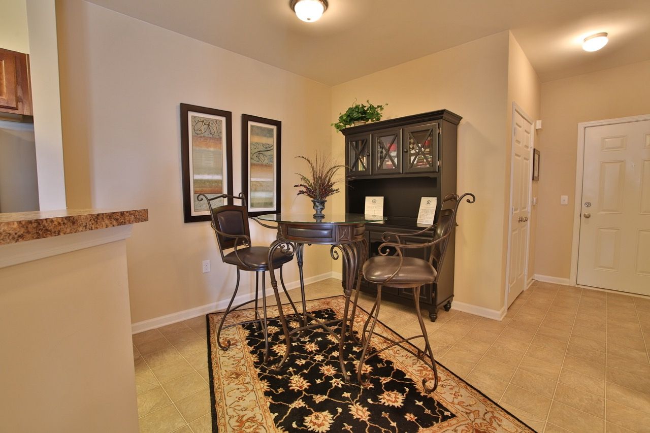 Indoor dining area with a round metal table and chairs, beige walls, and a decorative rug.