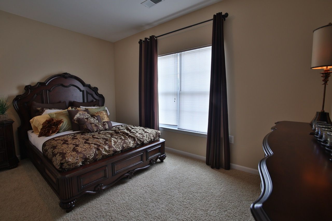 Bedroom with dark wooden bed and matching dresser, window with blinds.