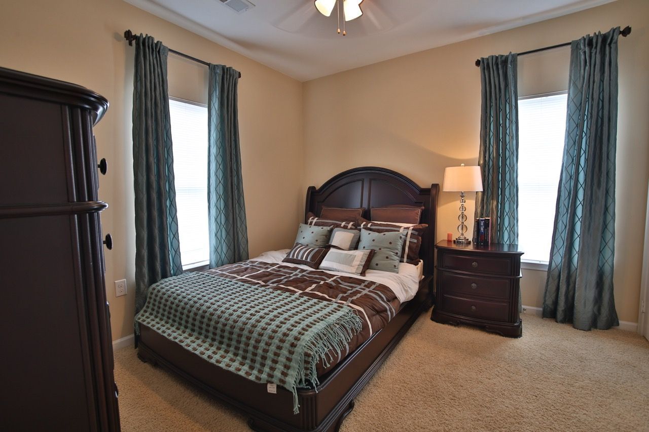 Bedroom with dark wood bed frame, matching dresser/nightstand, teal curtains, beige carpet.