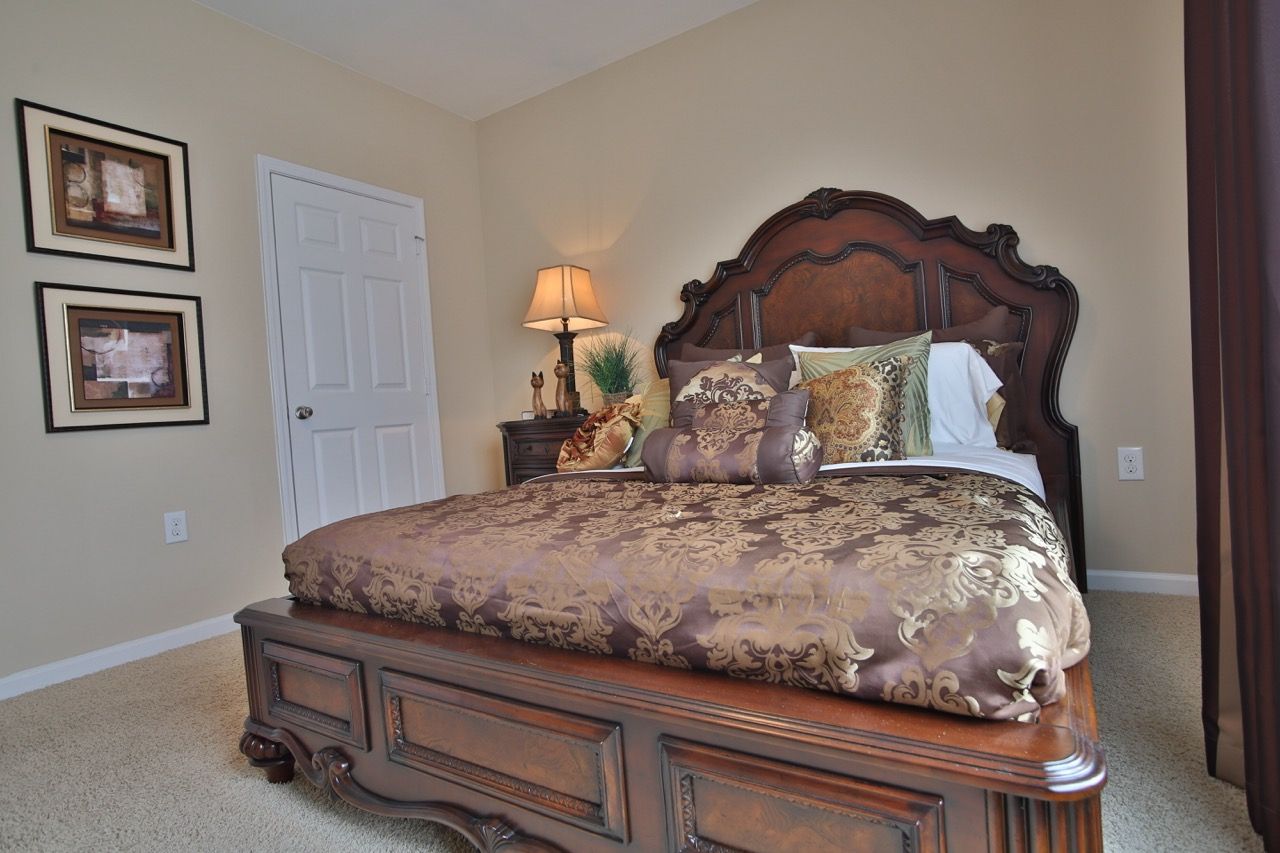 Bedroom with ornate dark wood bed, matching nightstand, lamp, and framed wall art.