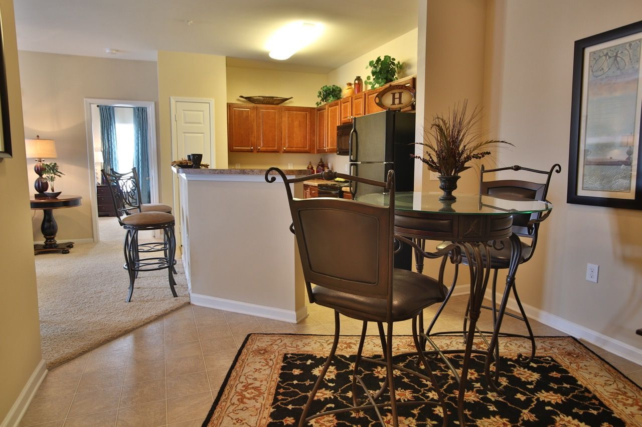 Open kitchen with a breakfast bar, glass-top table, and metal chairs in an apartment dining area.