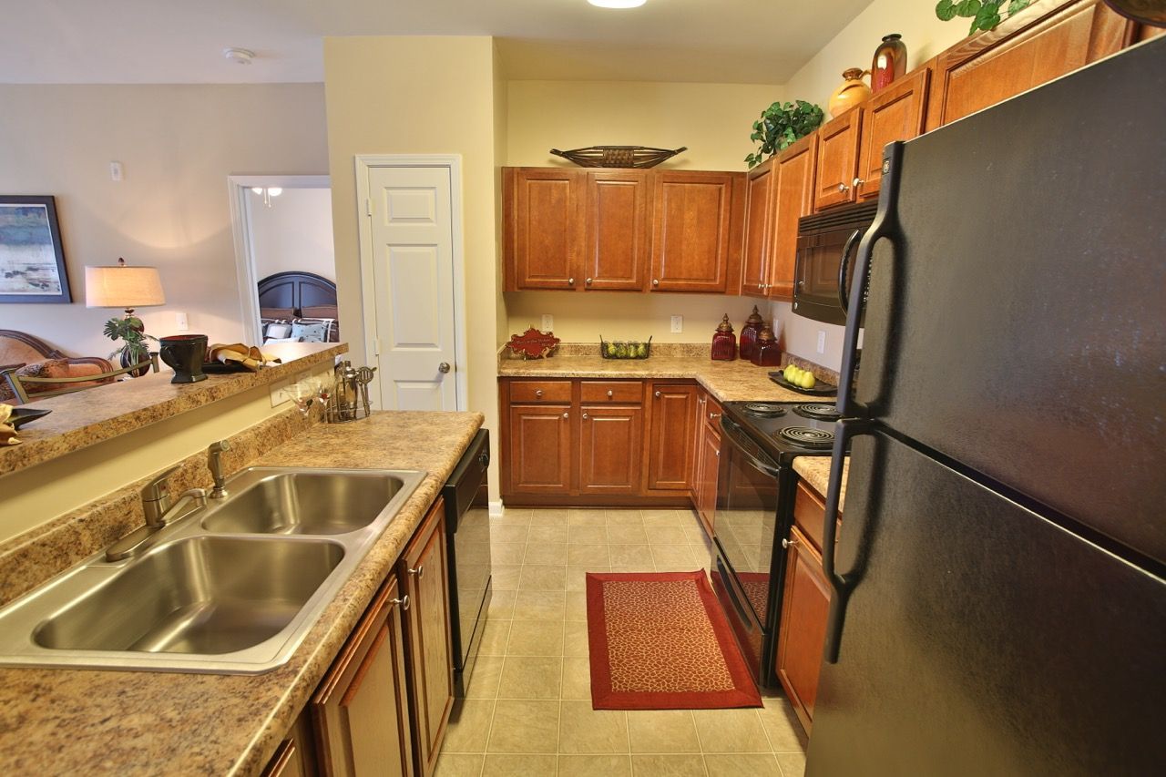 Apartment kitchen with brown cabinets, granite counters, double sink, and black appliances.