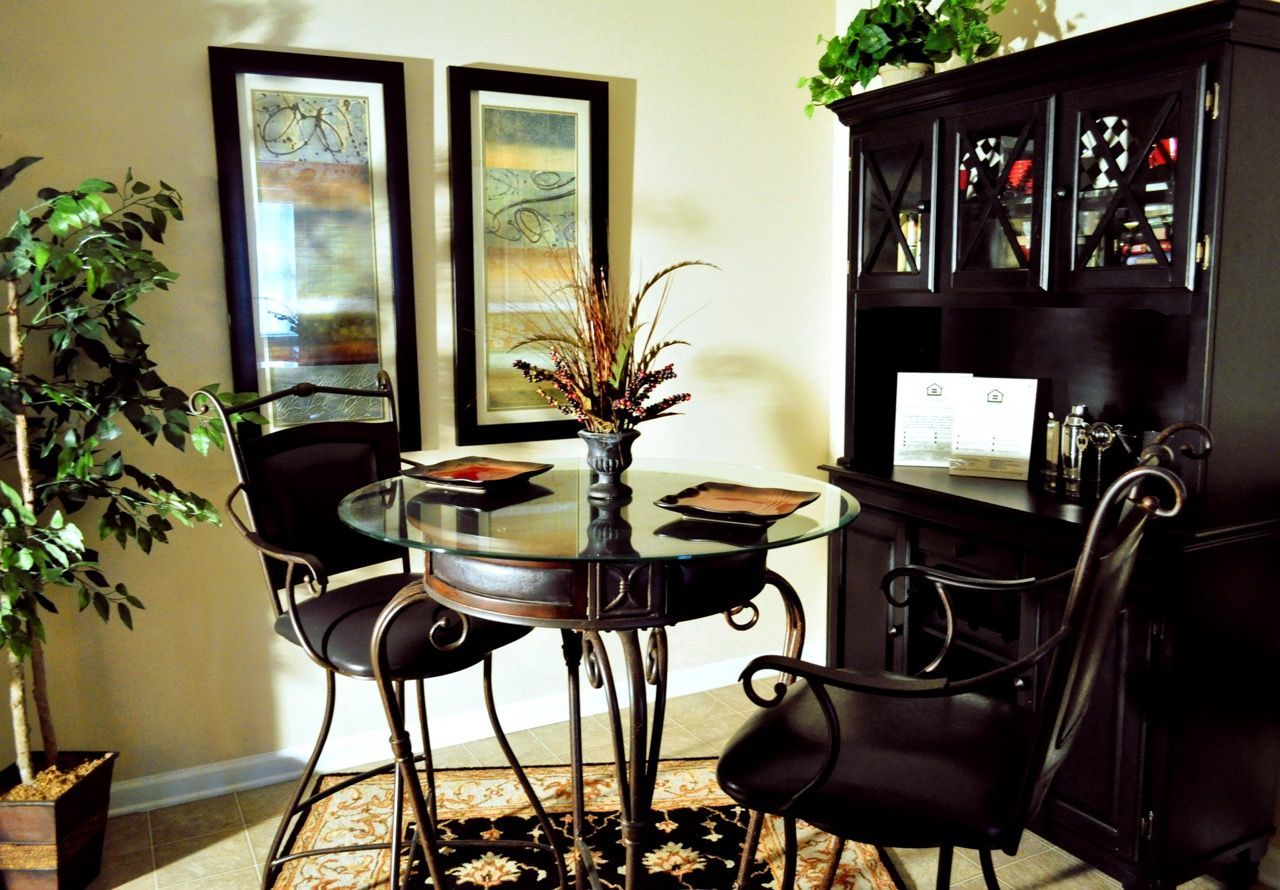 Interior of an apartment dining area with a glass round table, metal chairs, and a dark wood cabinet.
