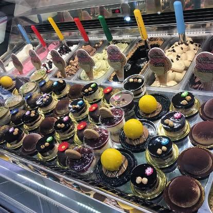 Una vetrina piena di una varietà di gusti di gelato artigianale, decorata con dolcetti di cioccolato e coni.