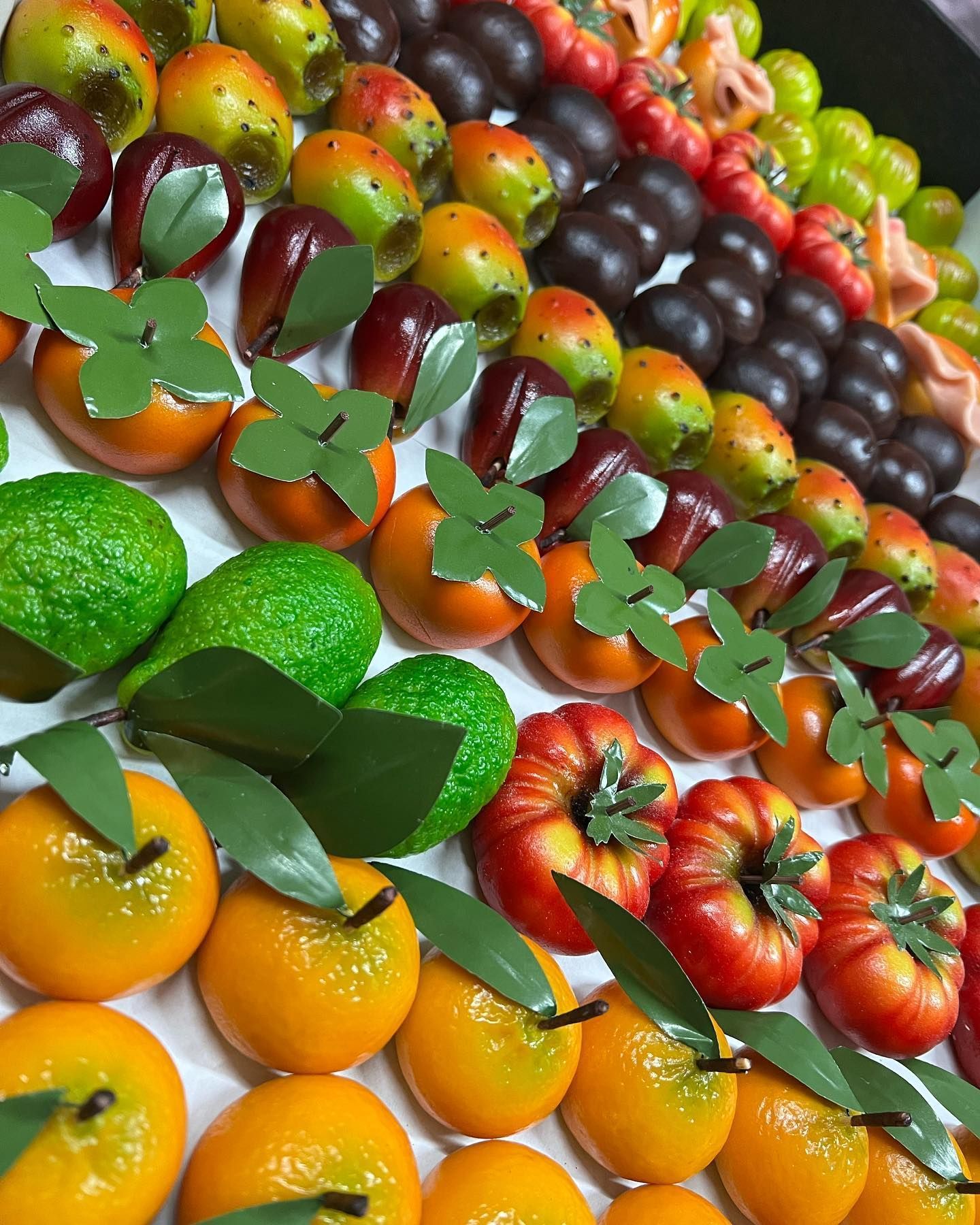 Una vista dall'alto di dolcetti di marzapane a forma di vari frutti, tra cui arance, lime e frutti di bosco scuri.