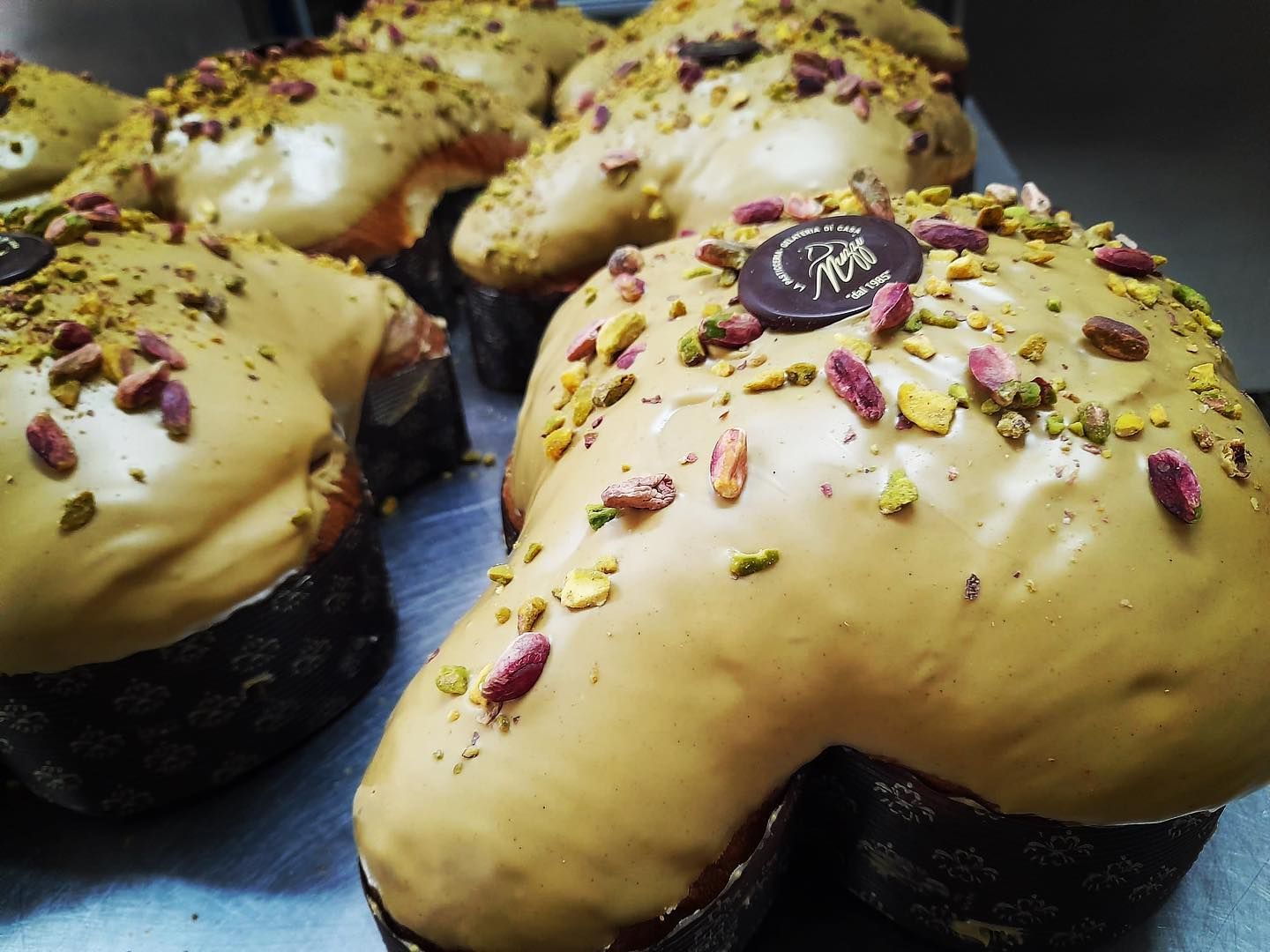 Diverse colomba a forma di colomba, ricoperte di glassa al pistacchio e pistacchi tritati, disposte su un vassoio di metallo.