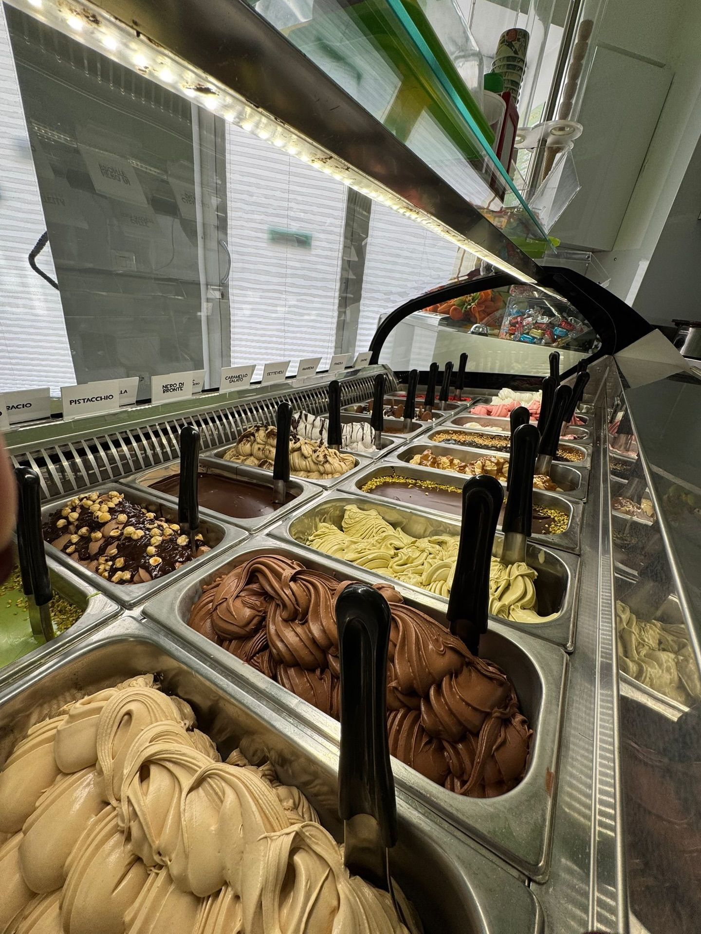 Una vetrina piena di gelati di vari gusti in contenitori di metallo, illuminata da una luce intensa.