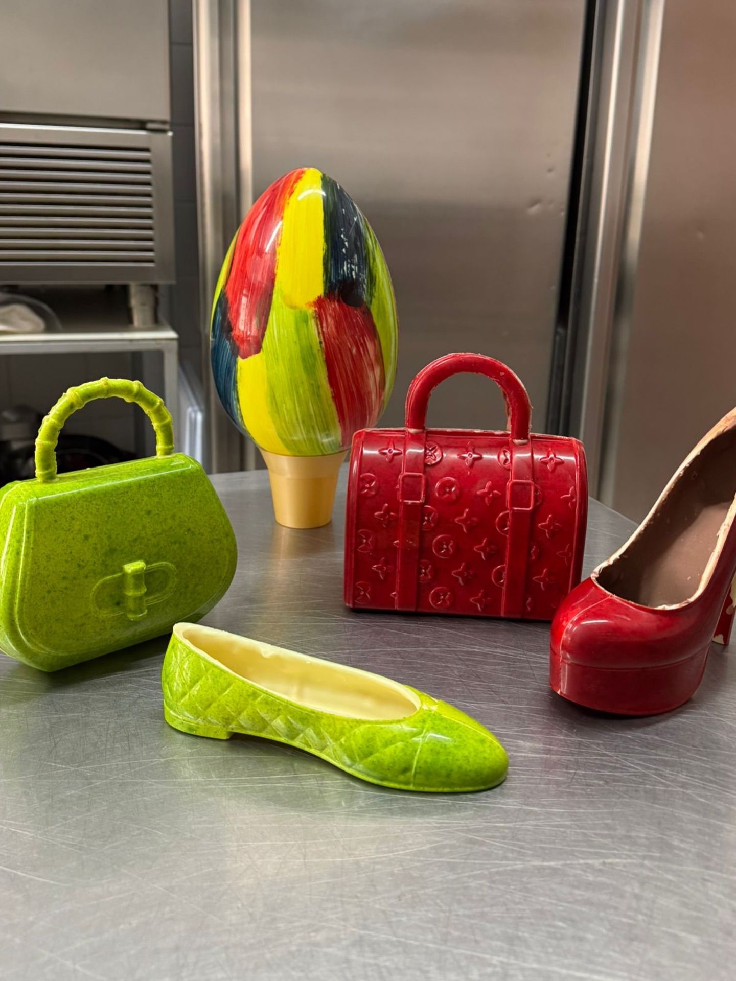 Statuette di cioccolato: un uovo di Pasqua colorato, una borsa e una ballerina verde lime, una borsetta rossa e una scarpa rossa con il tacco alto.