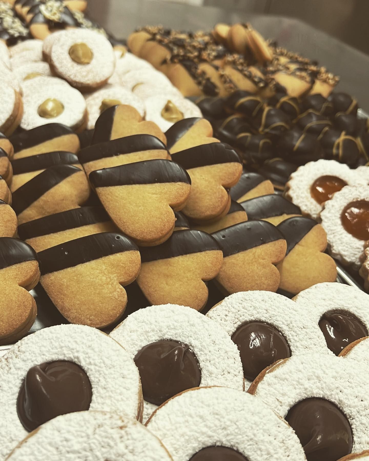 Un assortimento di biscotti di vario tipo, tra cui biscotti a forma di cuore ricoperti di cioccolato, biscotti rotondi ripieni di marmellata e ricoperti di zucchero a velo, e dolcetti al cioccolato.