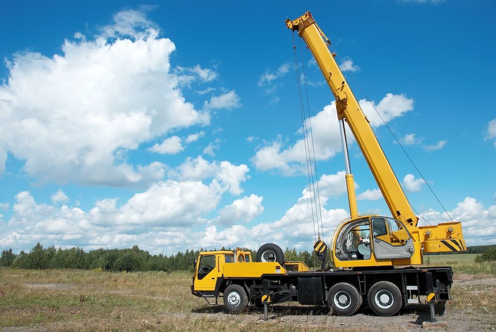 A Yellow Crane is Sitting on Top of a Truck in a Field — Smithys Crane Hire in Port Douglas, QLD