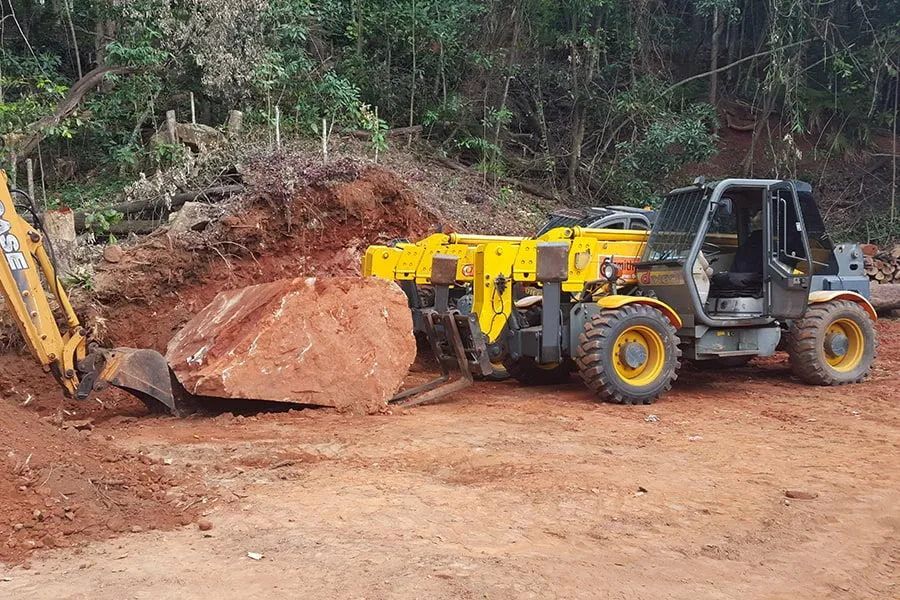 Yellow Tractor Is Carrying a Large Rock in A Dirt Field — Smithys Crane Hire in Trinity Beach, QLD