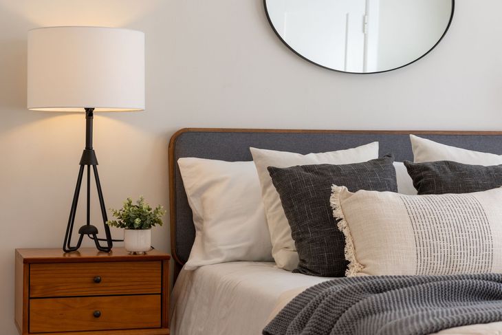 A bedroom with a bed , nightstand , lamp and mirror.