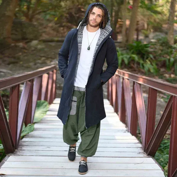 Un homme portant un manteau noir et un pantalon vert se tient debout sur un pont en bois.