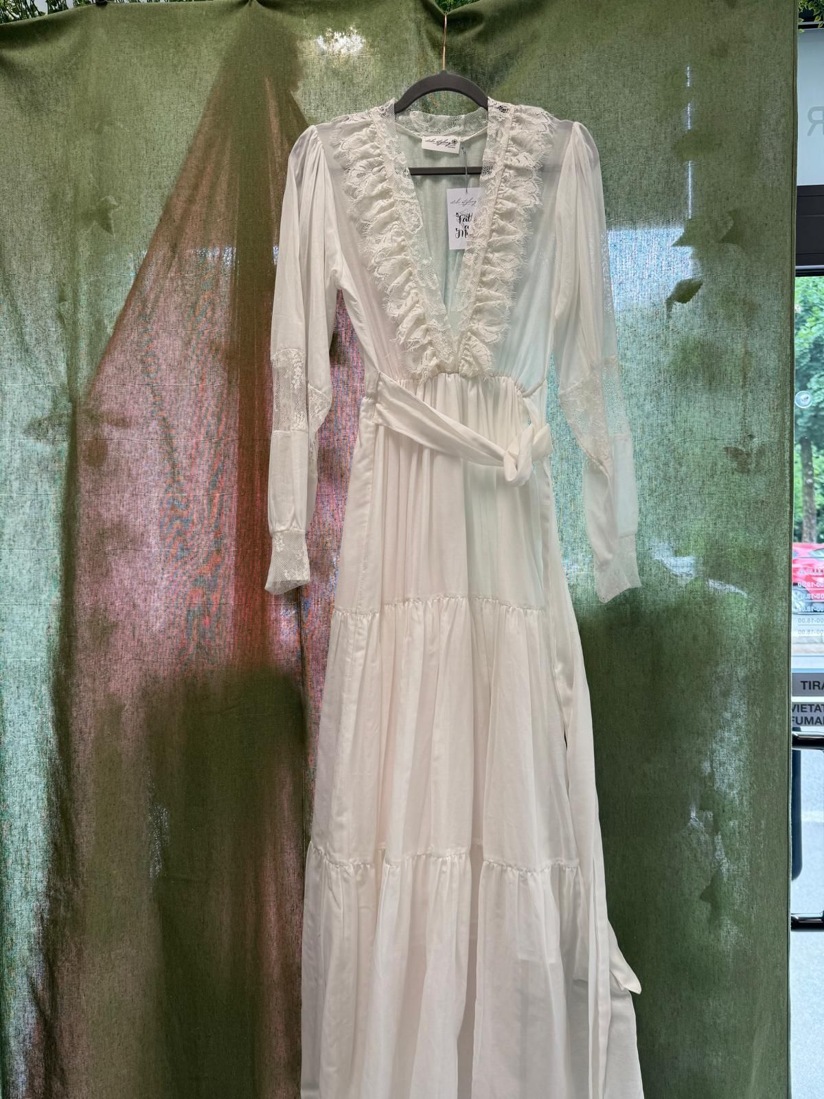 Ad una gruccia è appeso un abito bianco con maniche lunghe e volant.