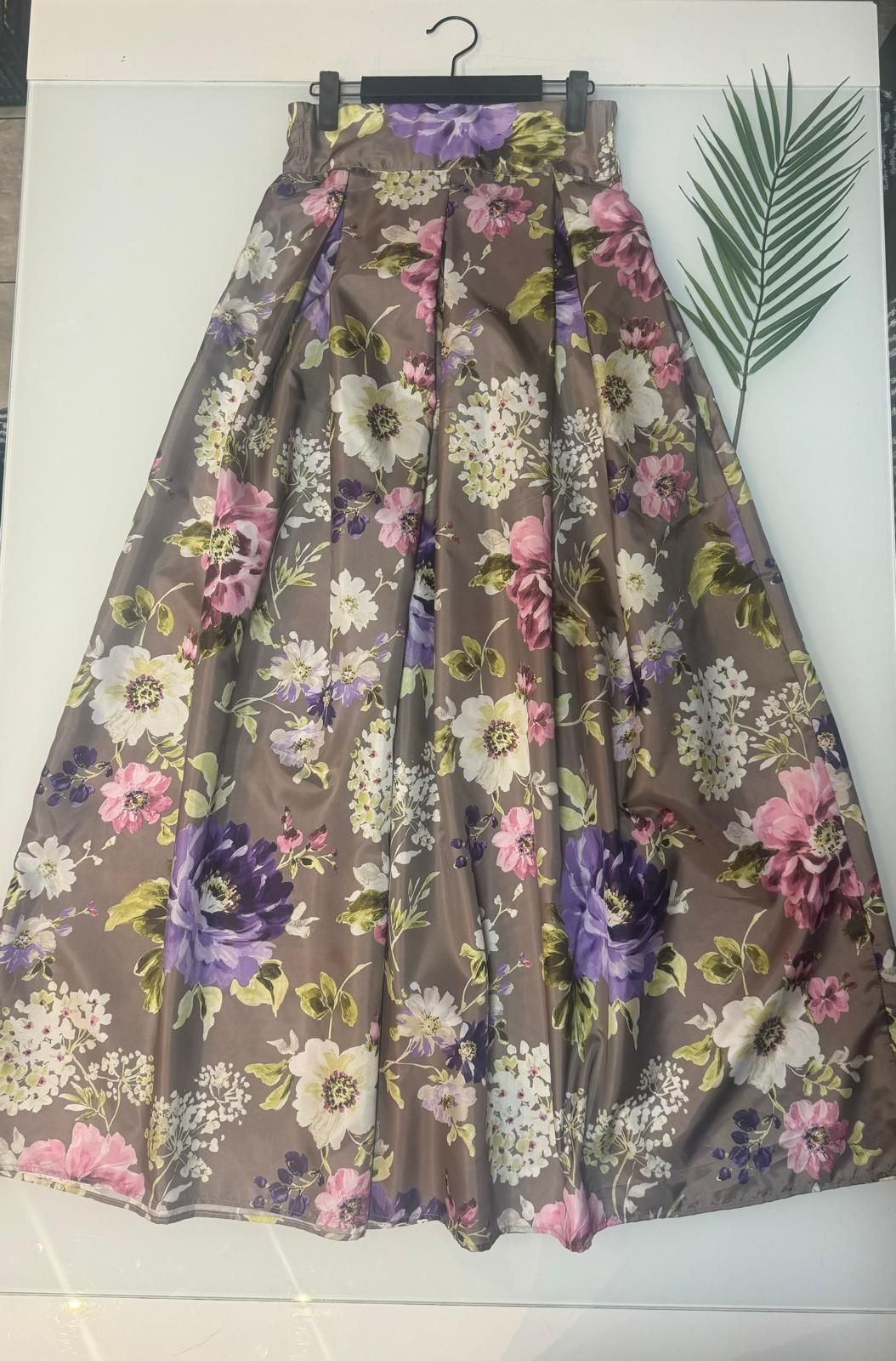 Una gonna floreale è appesa a una gruccia accanto a una foglia di palma.