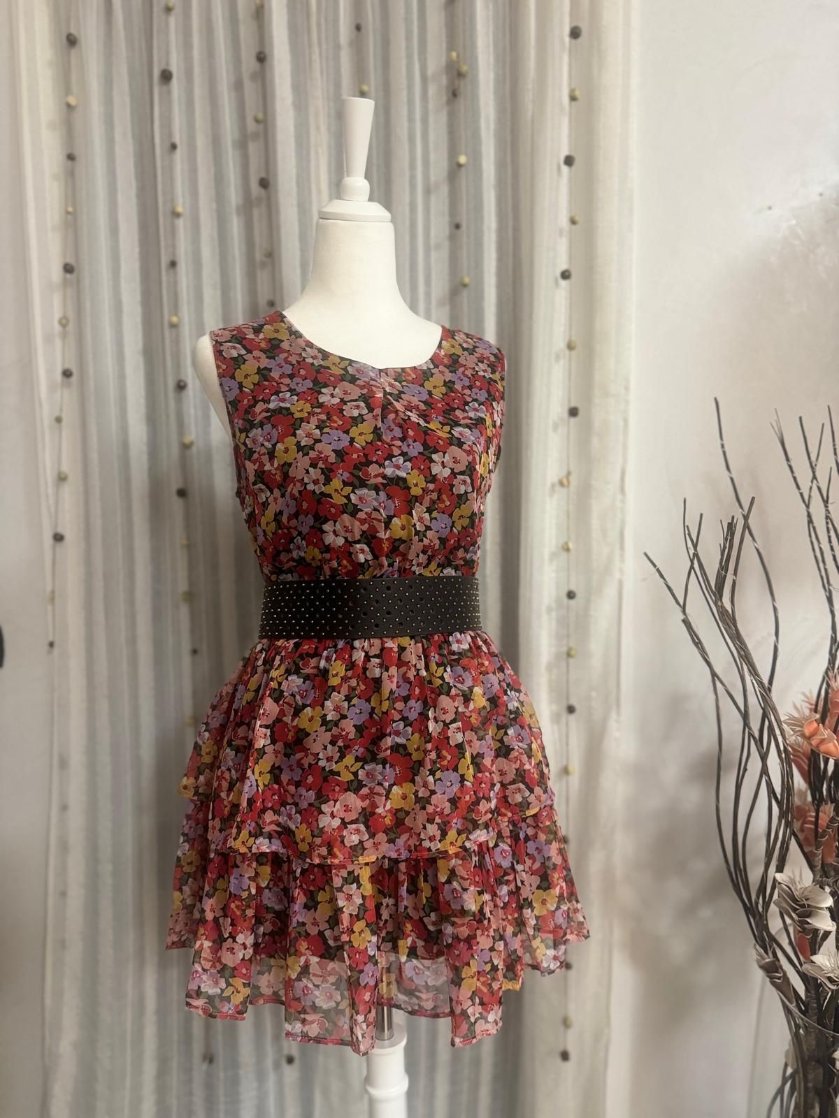 Un abito floreale è su un manichino davanti a una tenda bianca.