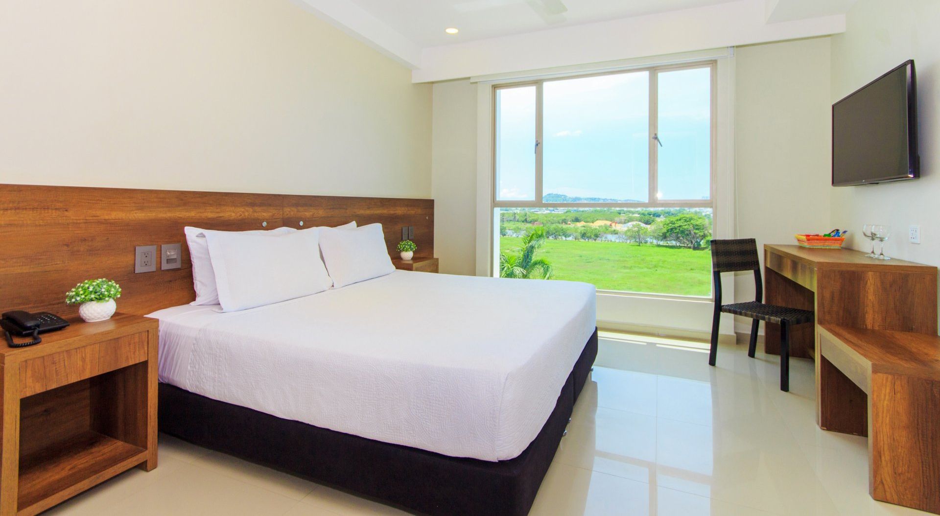 Una habitación de hotel con cama king size, escritorio, silla y televisión.