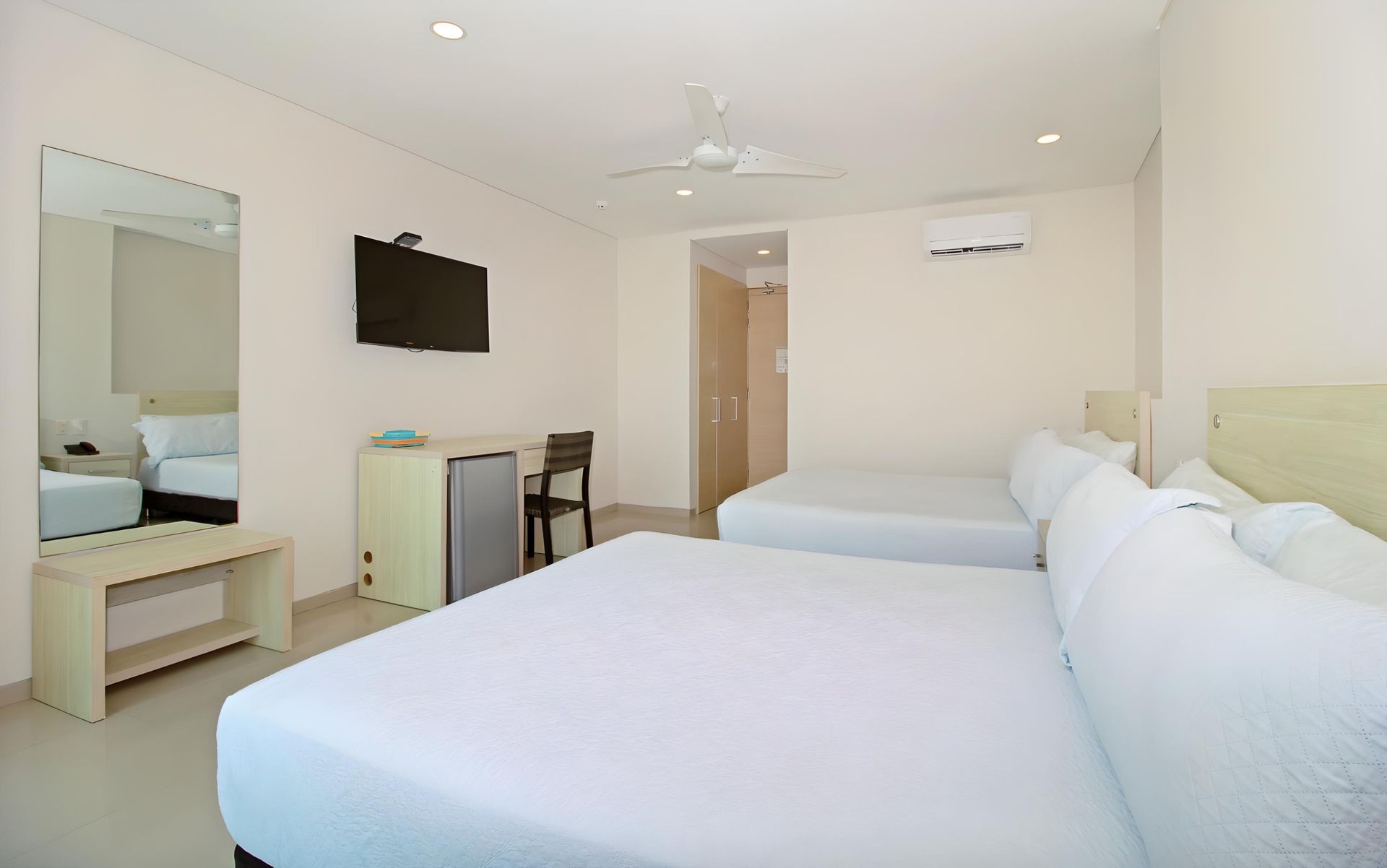 Una habitación de hotel con dos camas, un escritorio, una televisión y un ventilador de techo.