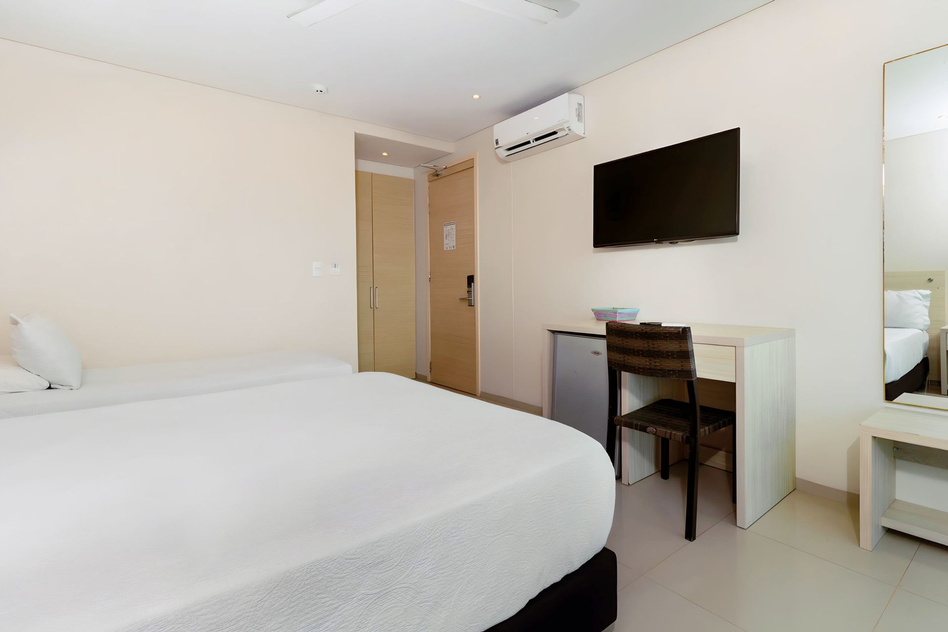 Una habitación de hotel con cama, escritorio, televisión y espejo.