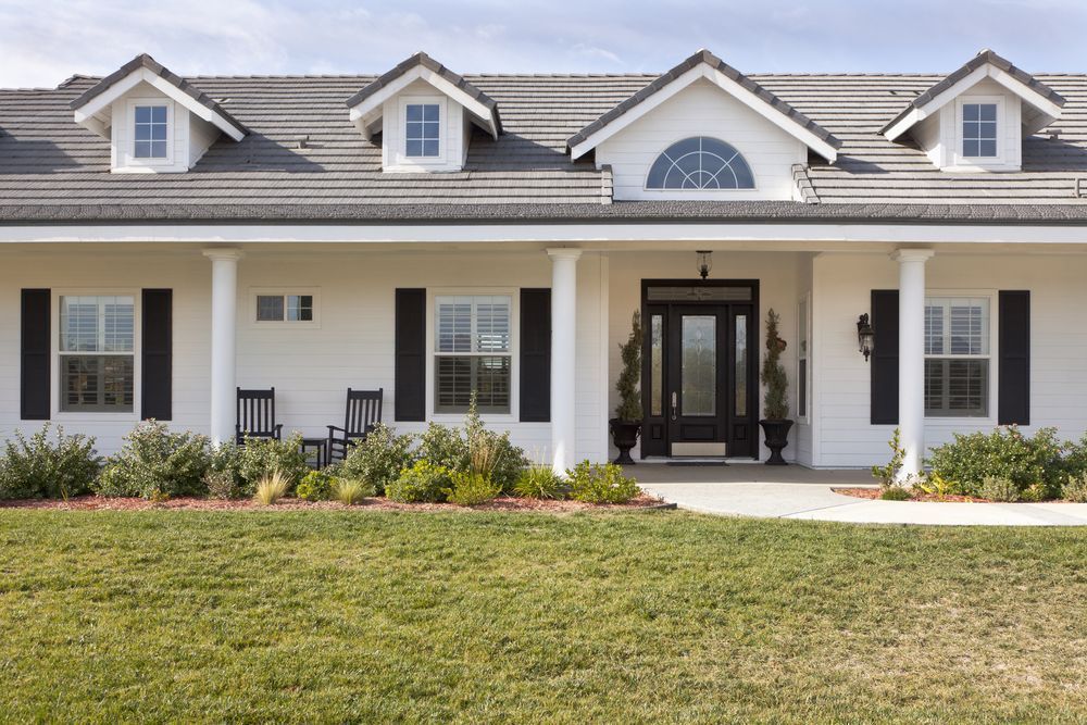 A large white house with black shutters and a large lawn in front of it.
