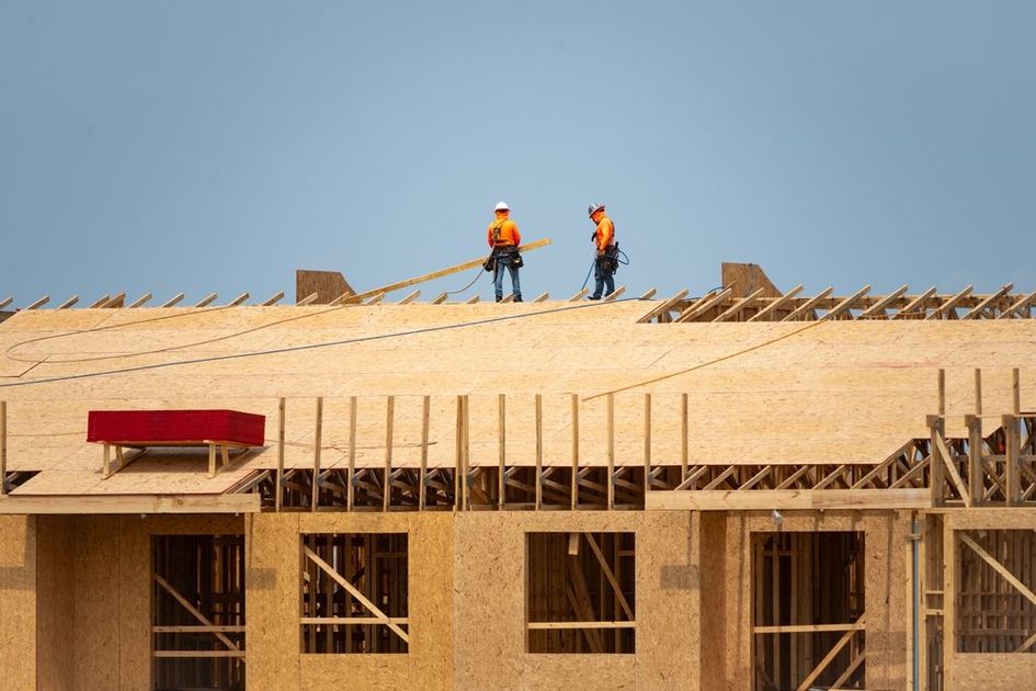 Two construction workers are working on the roof of a building under construction.