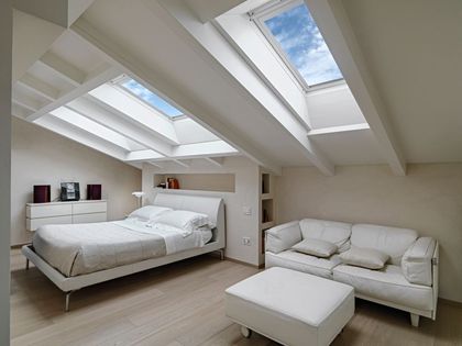 White bedroom with bed, couch, and skylights in sloped ceiling.