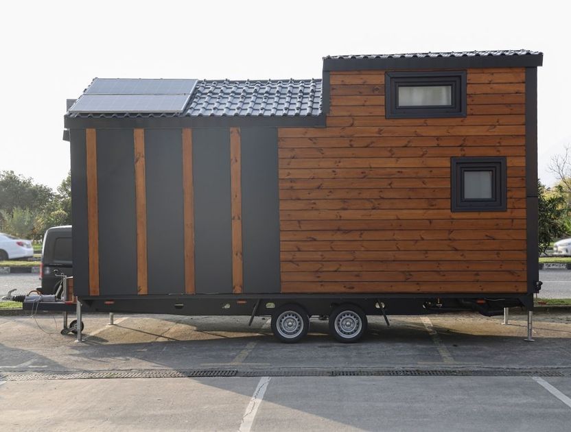 A tiny house on wheels is parked in a parking lot.