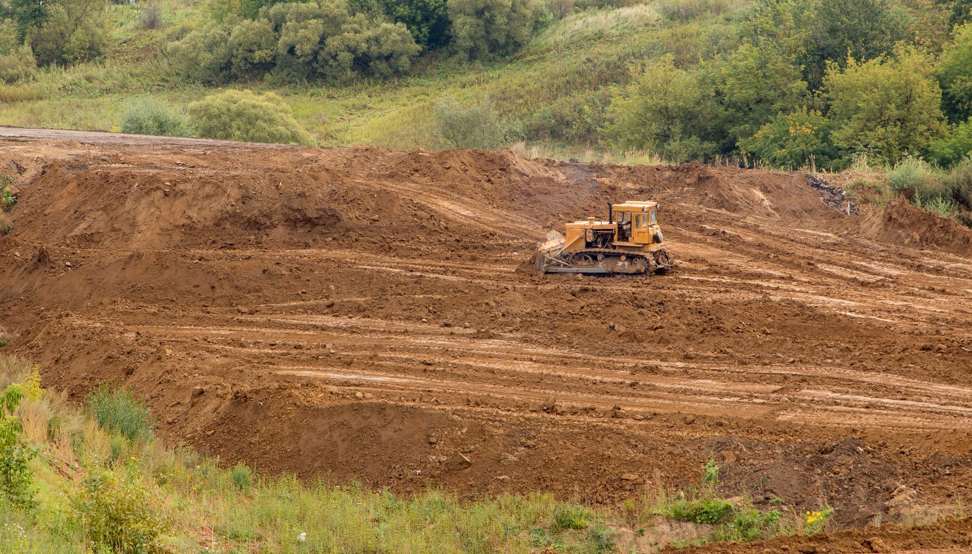 Bulldozer grading a large dirt hillside with green vegetation in the background