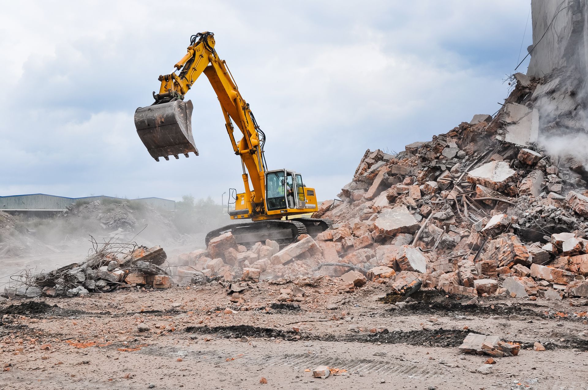 Yellow excavator demolishing rubble beside a partially destroyed wall, with dust rising over a debris field. Yellow excavator demolishing rubble beside a partially destroyed wall, with dust rising over a debris field.