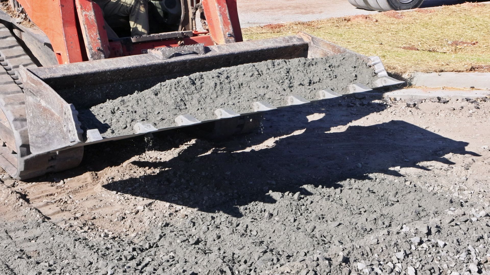 Construction vehicle dumping wet concrete onto a dirt surface