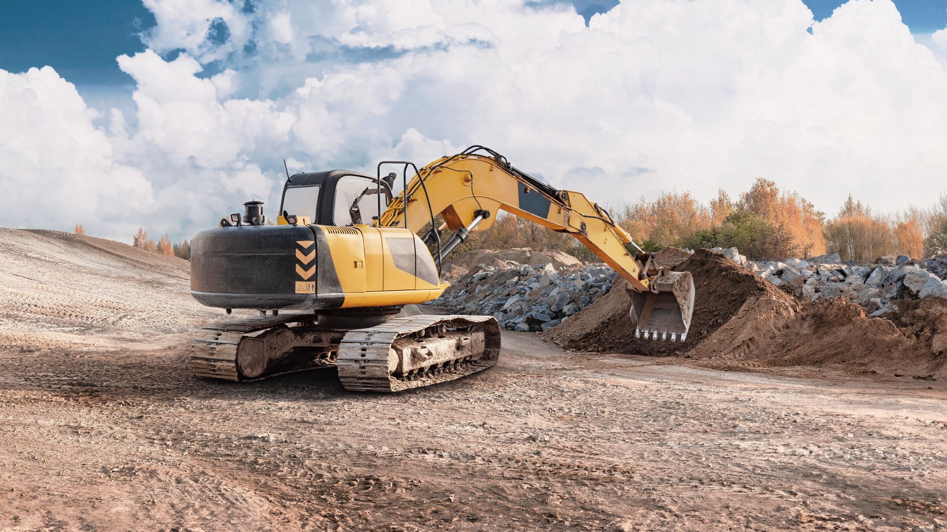 Yellow excavator digging dirt at a construction site under a cloudy sky