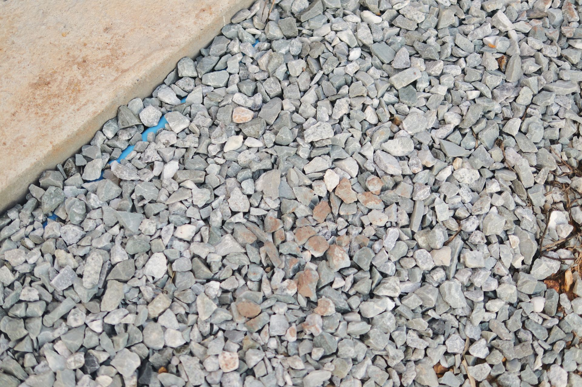 Gray gravel beside a beige wall, with a few small blue and tan stones scattered among the rocks