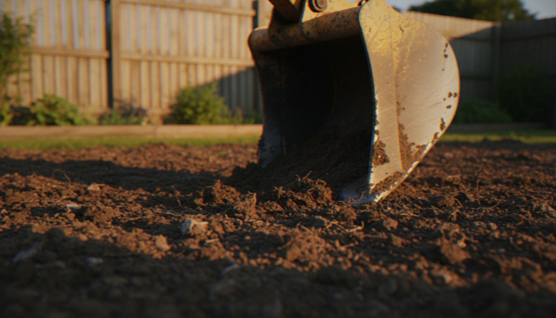Close-up of a backhoe bucket digging into loose soil in a yard