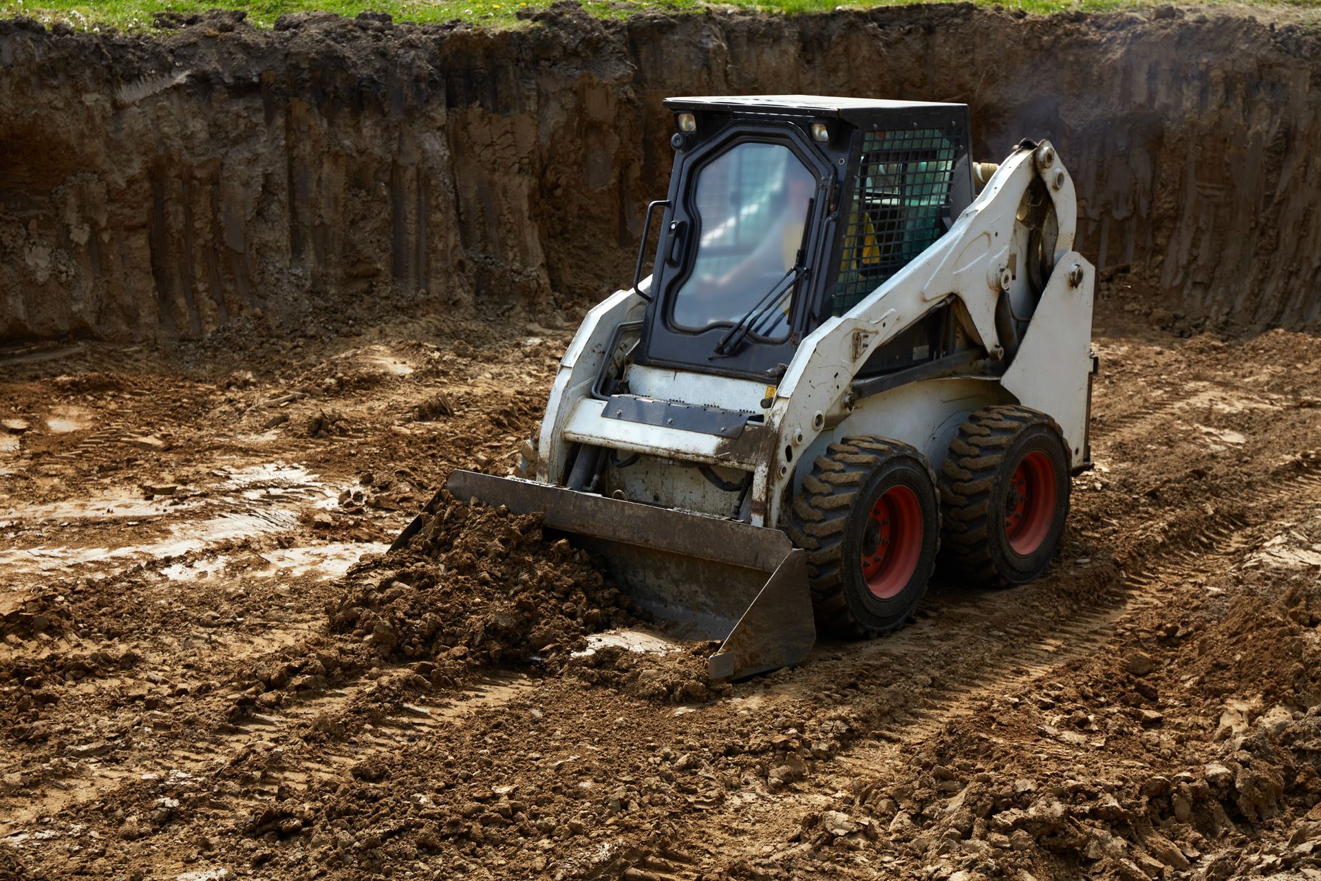 White skid-steer loader moving dirt in a muddy excavation site
