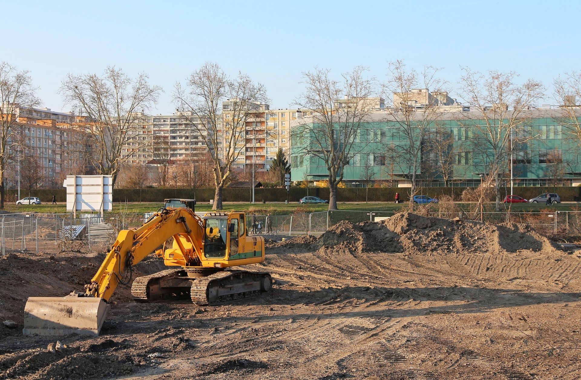 Yellow excavator at a construction site with dirt piles and apartment buildings in the background