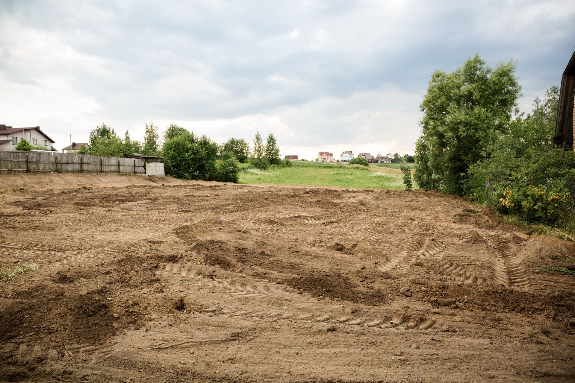 Cleared dirt lot beside green fields and trees under a cloudy sky Cleared dirt lot beside green fields and trees under a cloudy sky