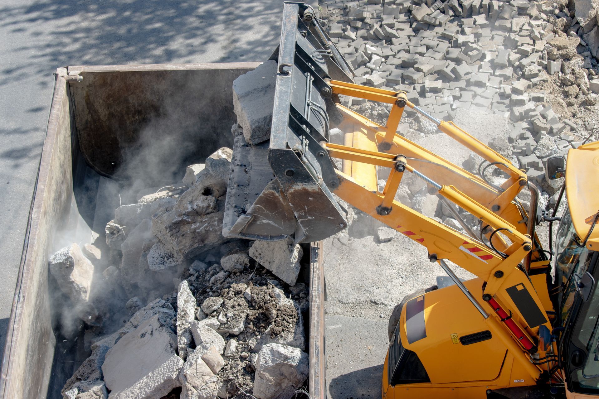 Yellow excavator dumping rubble into a large concrete pit, with dust rising around it. Yellow excavator dumping rubble into a large concrete pit, with dust rising around it.
