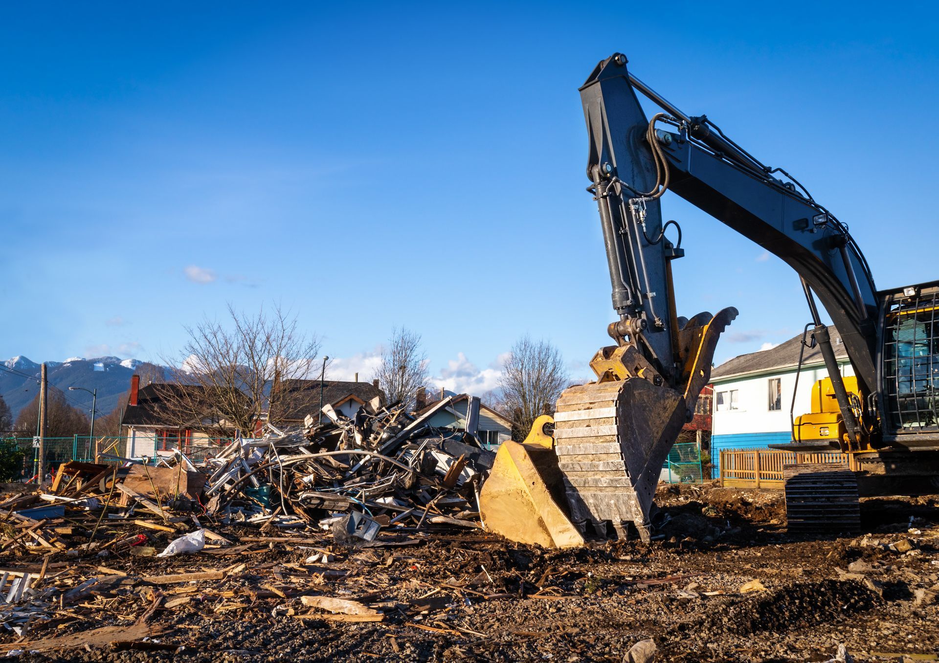Excavator clearing rubble at a demolition site under a clear blue sky