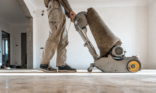 Worker sanding a hardwood parquet floor with a floor grinder