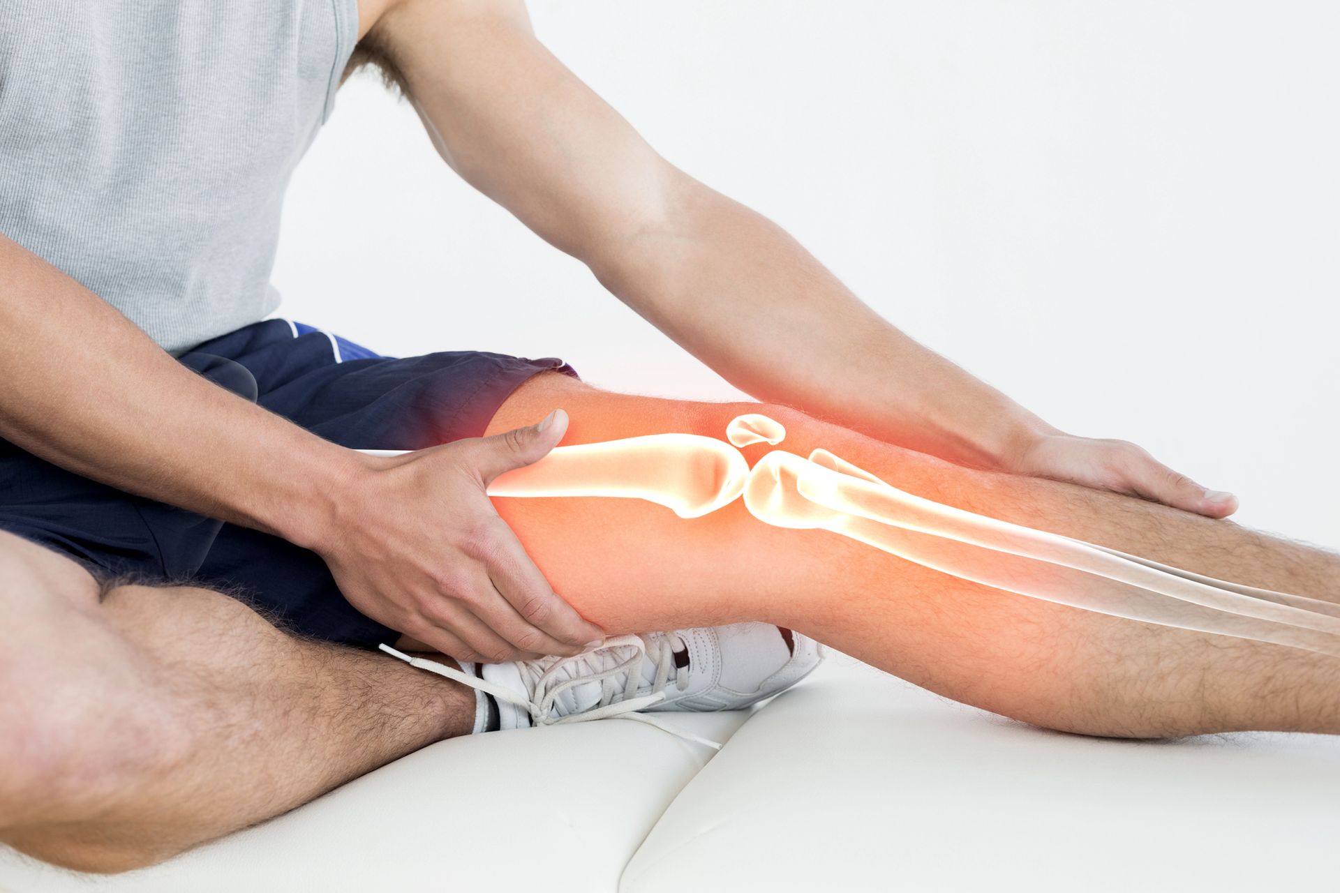 Un hombre está sentado en una cama sujetándose la rodilla con dolor.