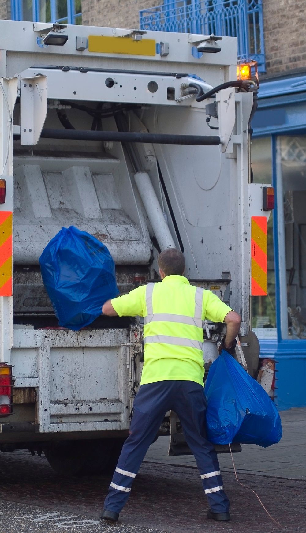A man in a yellow vest is loading garbage into a garbage truck.