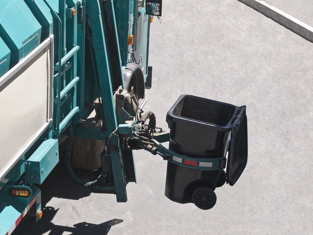 A garbage truck with a black trash can attached to it