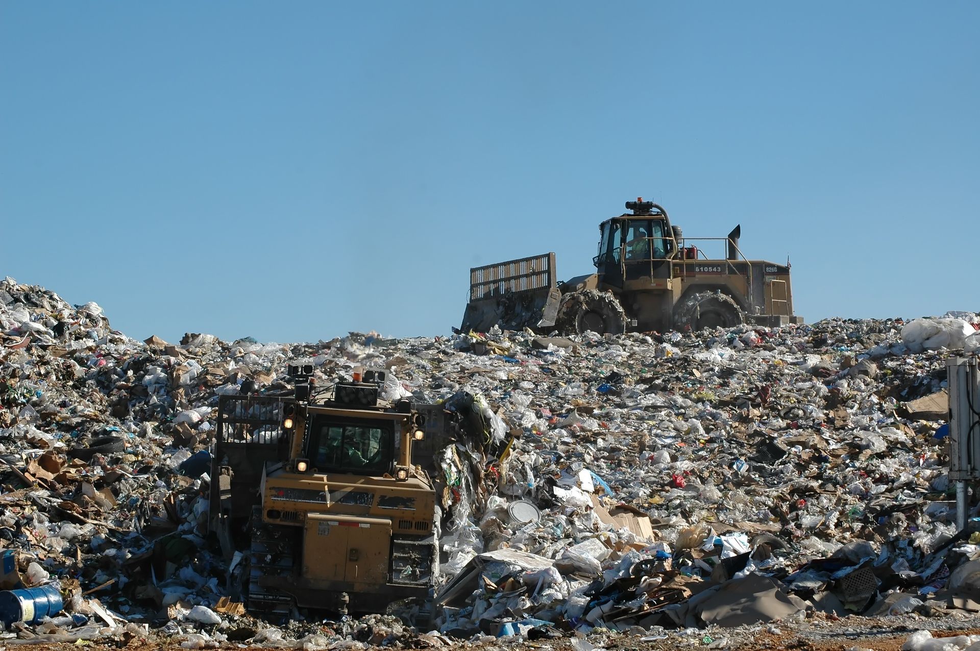 Two bulldozers are working on a pile of trash.