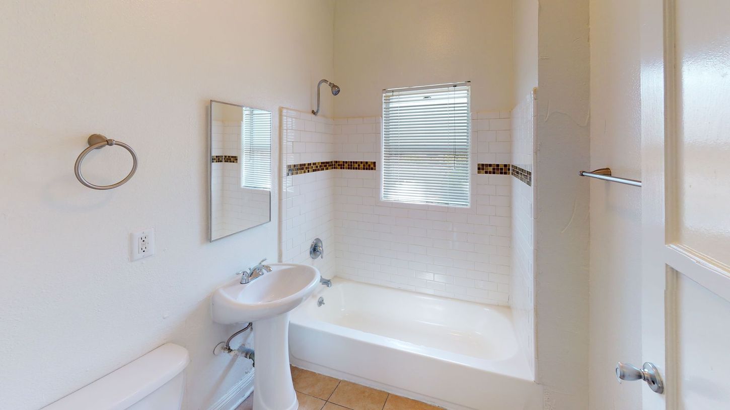 Bathroom with white walls, tub, pedestal sink, mirror, and a small window.